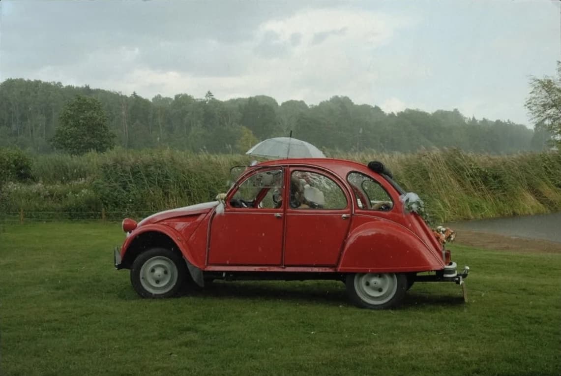 En röd Citroën 2CV med ett paraply ur taket i regnet
