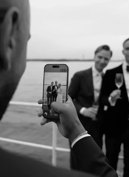 En gäst fotograferar brudgummen med mobilen, i svartvitt